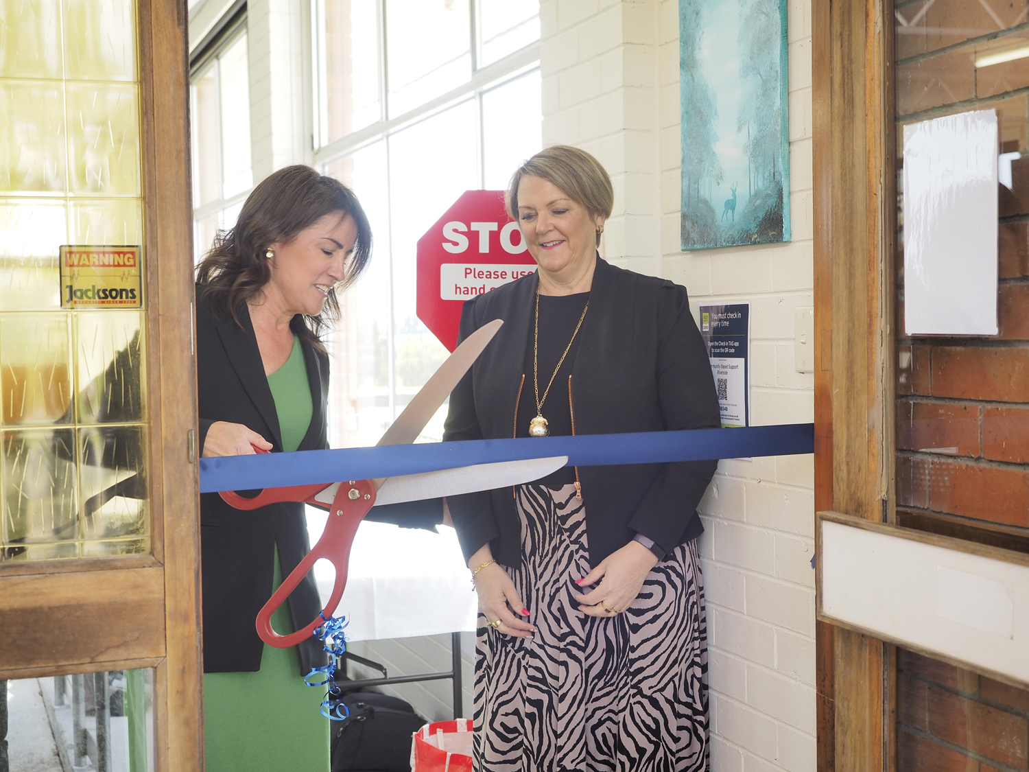 A woman cuts a blue ribbon over a doorway with a large scissors