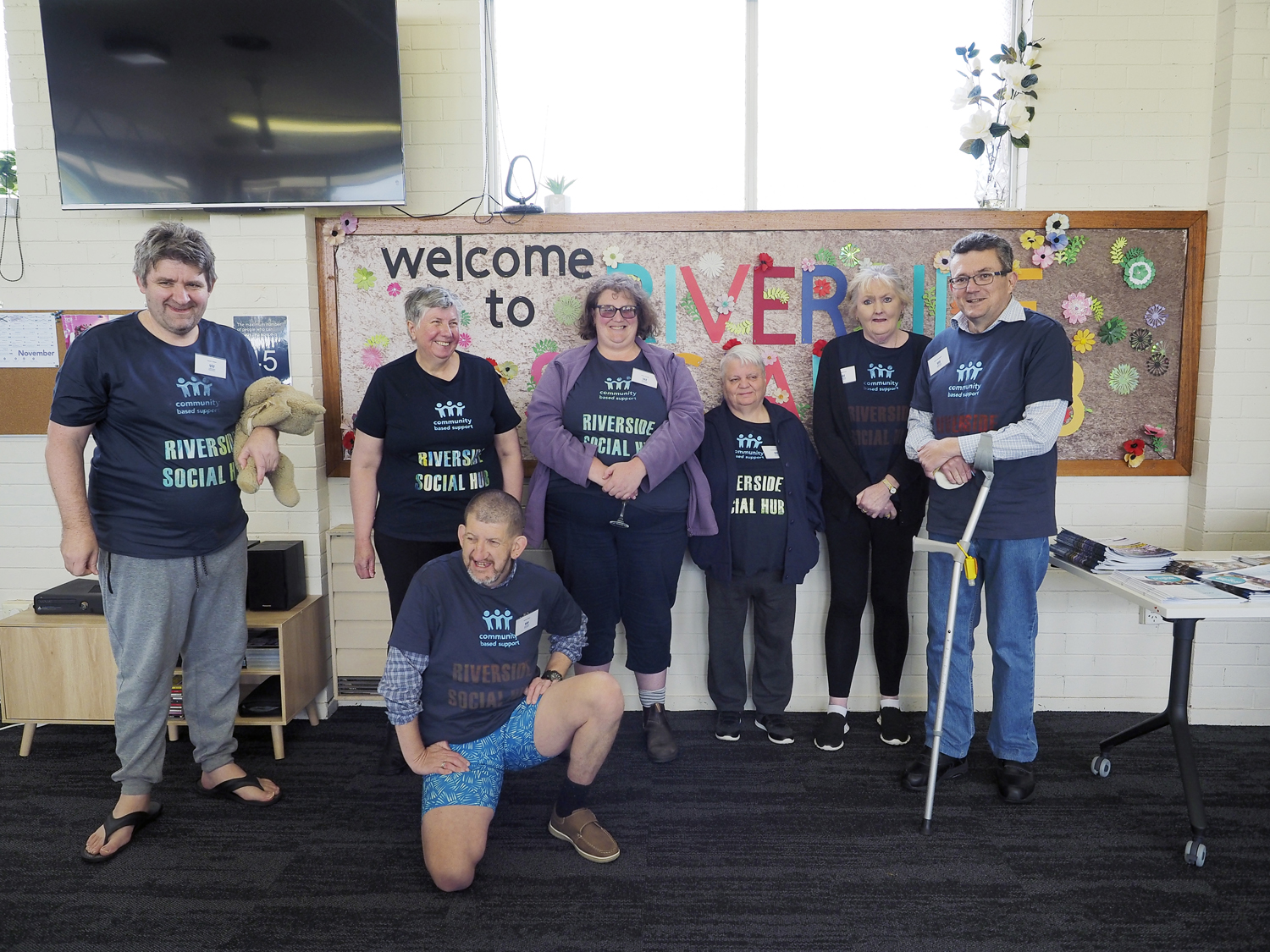 A group of people in matching t-shirts pose for a photo in front of a handmade sign