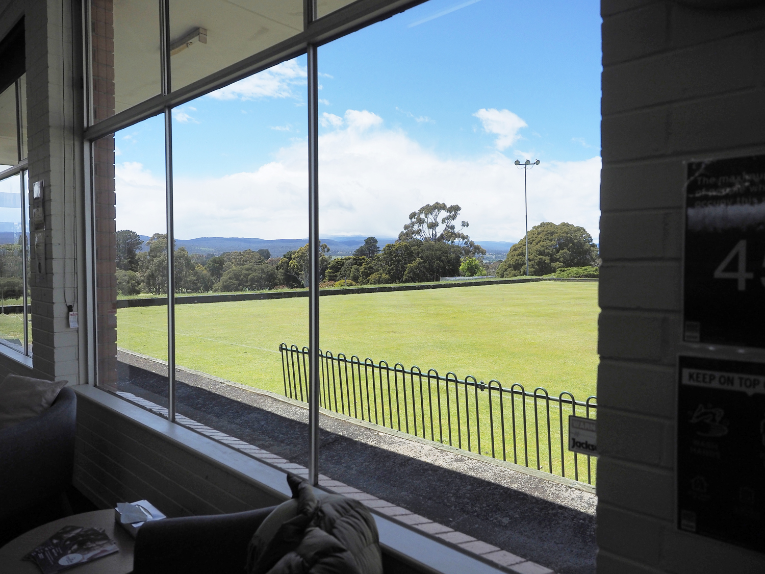 A view looking out a window to a bowls green and trees and hills in the background
