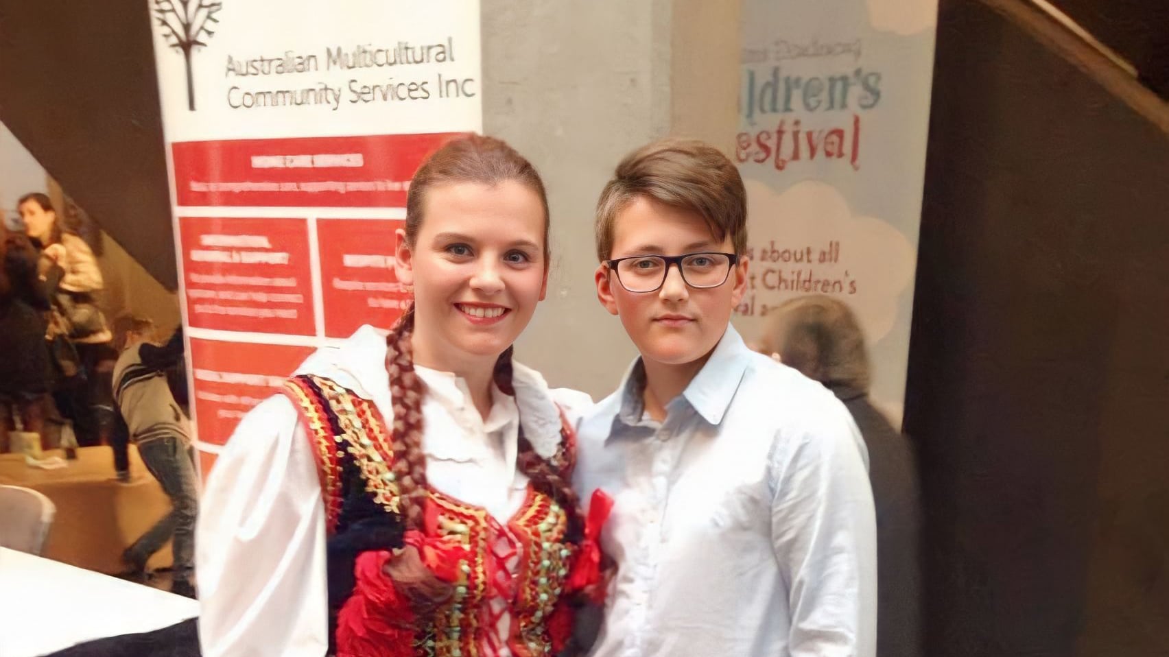 A woman in traditional Polish dress poses for a photo with a young man in white shirt and glasses