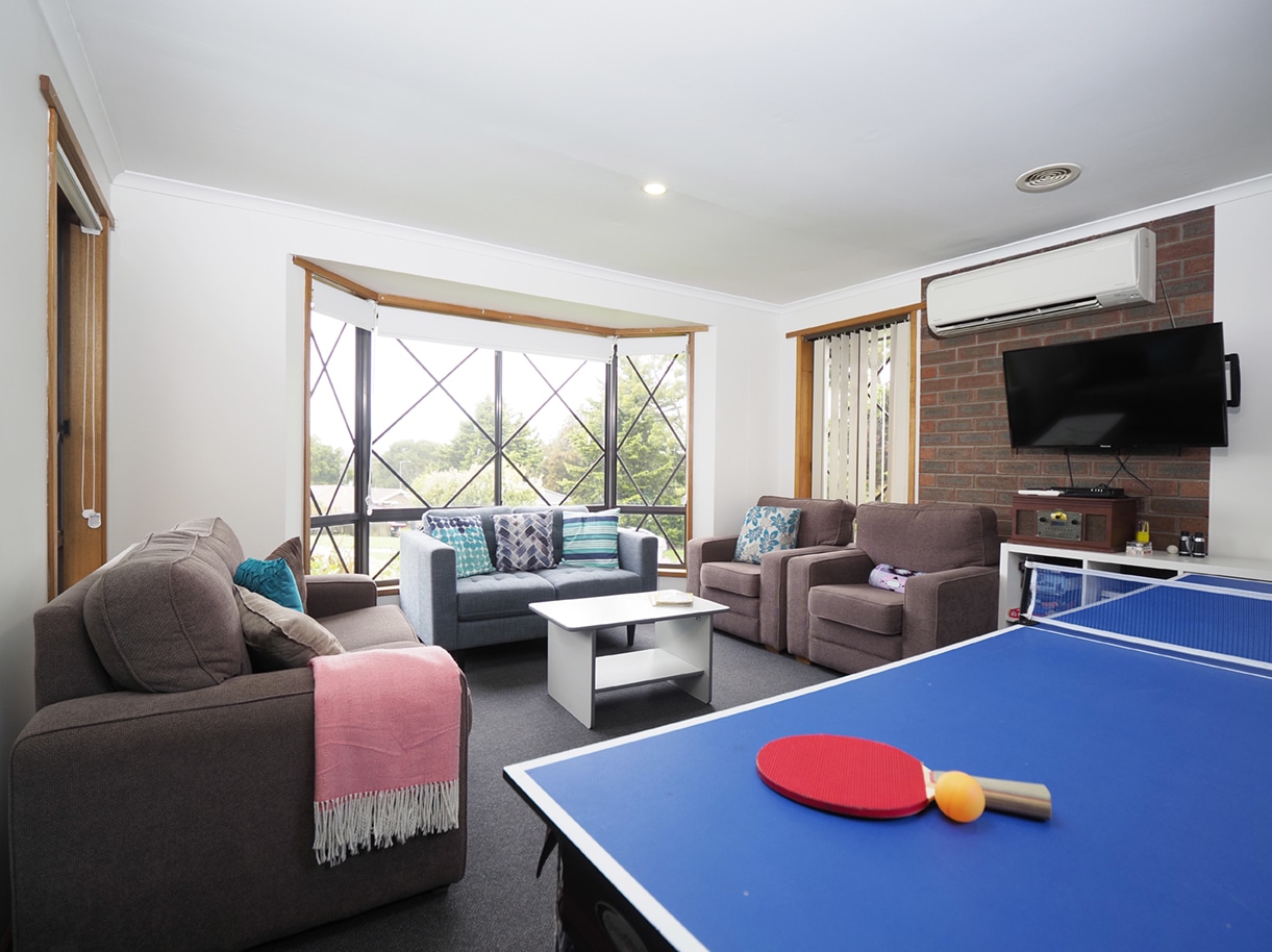 A living area with couches with a table tennis table in the foreground