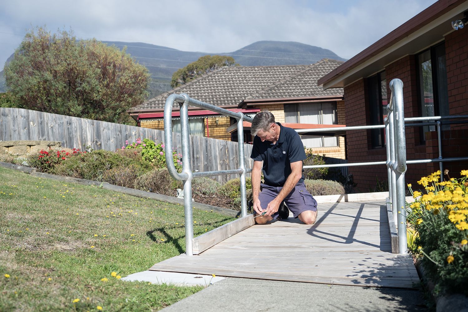 A worker installs a handrail on a concrete access ramp outside a home, improving safety and accessibility for an older resident.