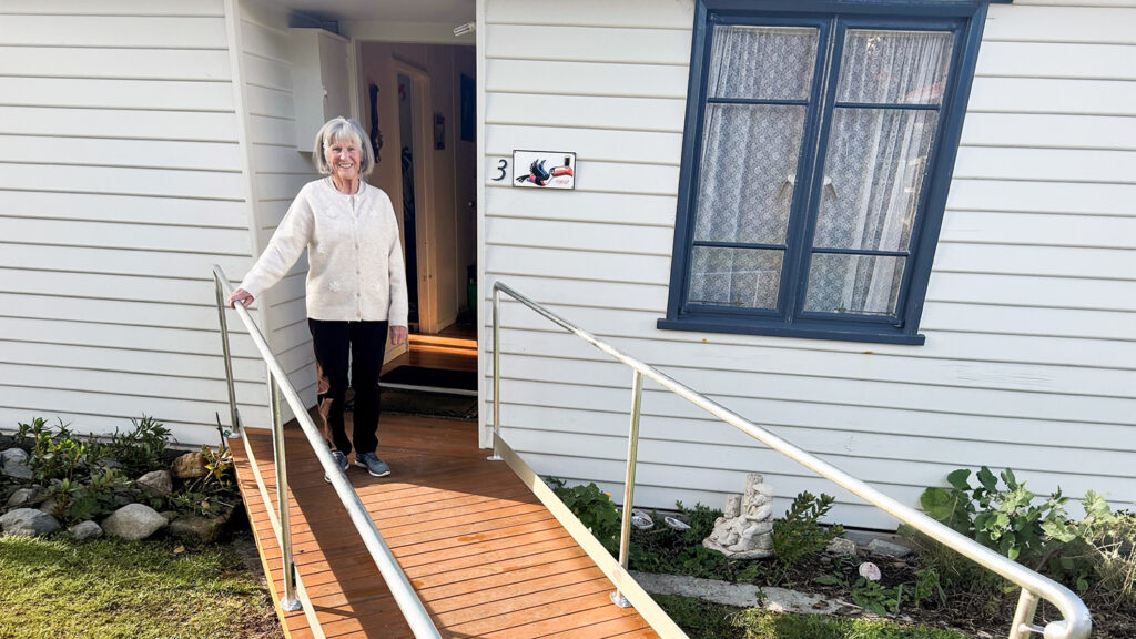 Bernadette standing on a newly installed access ramp outside her home, showing how home modifications support safer and more independent living.